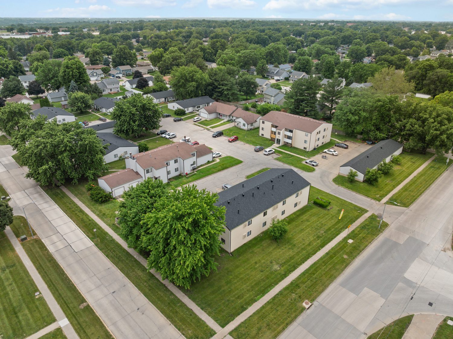 Aerial view of East Park in summer, the three-story and two-story apartment buildings at the back, single-story fourplexes and a garage building in front, with mature trees between them.