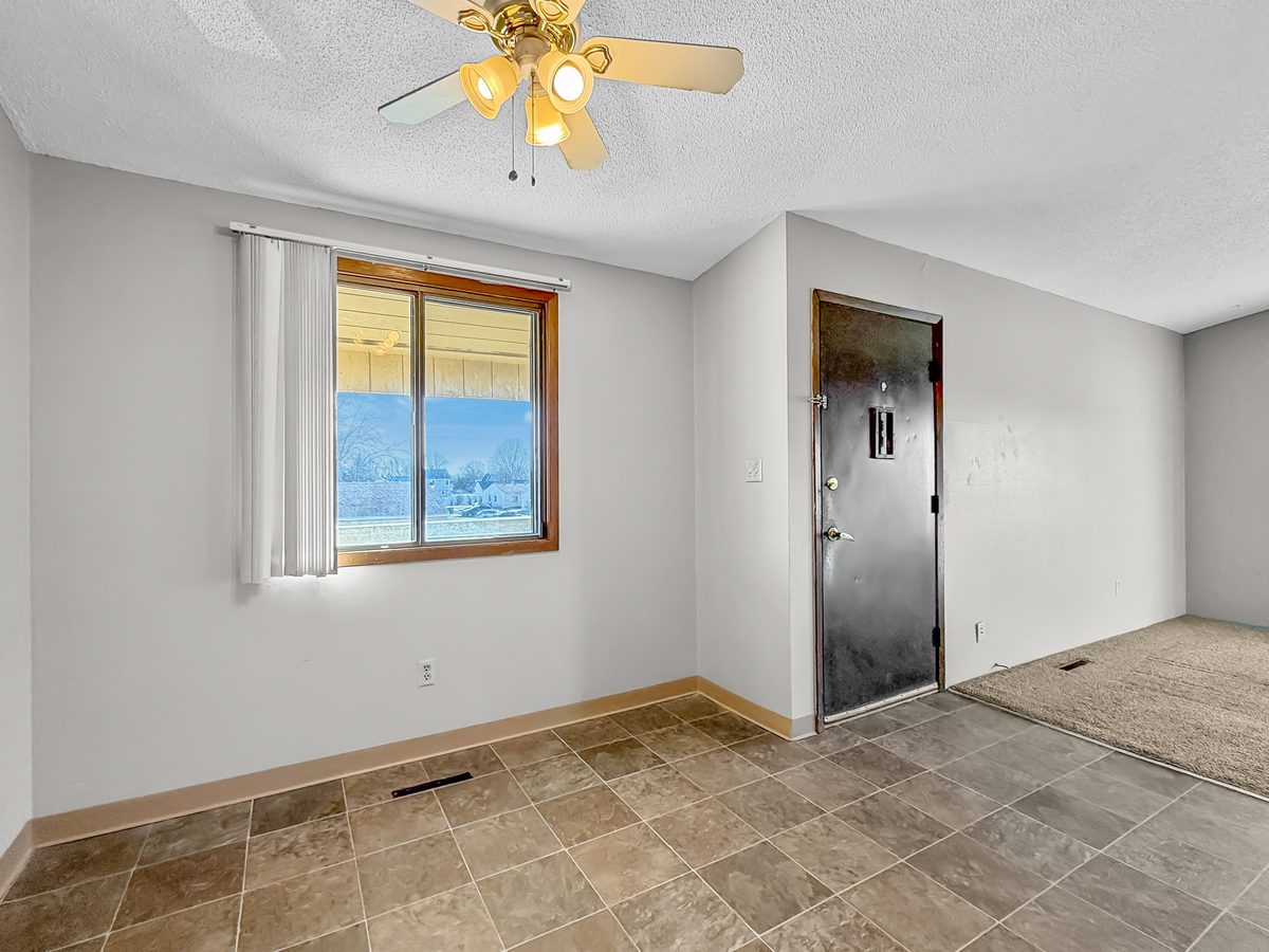 The living room of a renovated two bedroom apartment in the eight-unit building, with a vaulted ceiling, a ceiling fan, grey walls and a window with curtains.