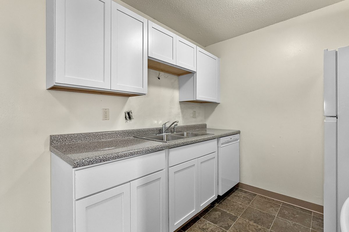 A renovated fourplex kitchen with white cabinets, a grey countertop, a double sink and tile-look vinyl floor.