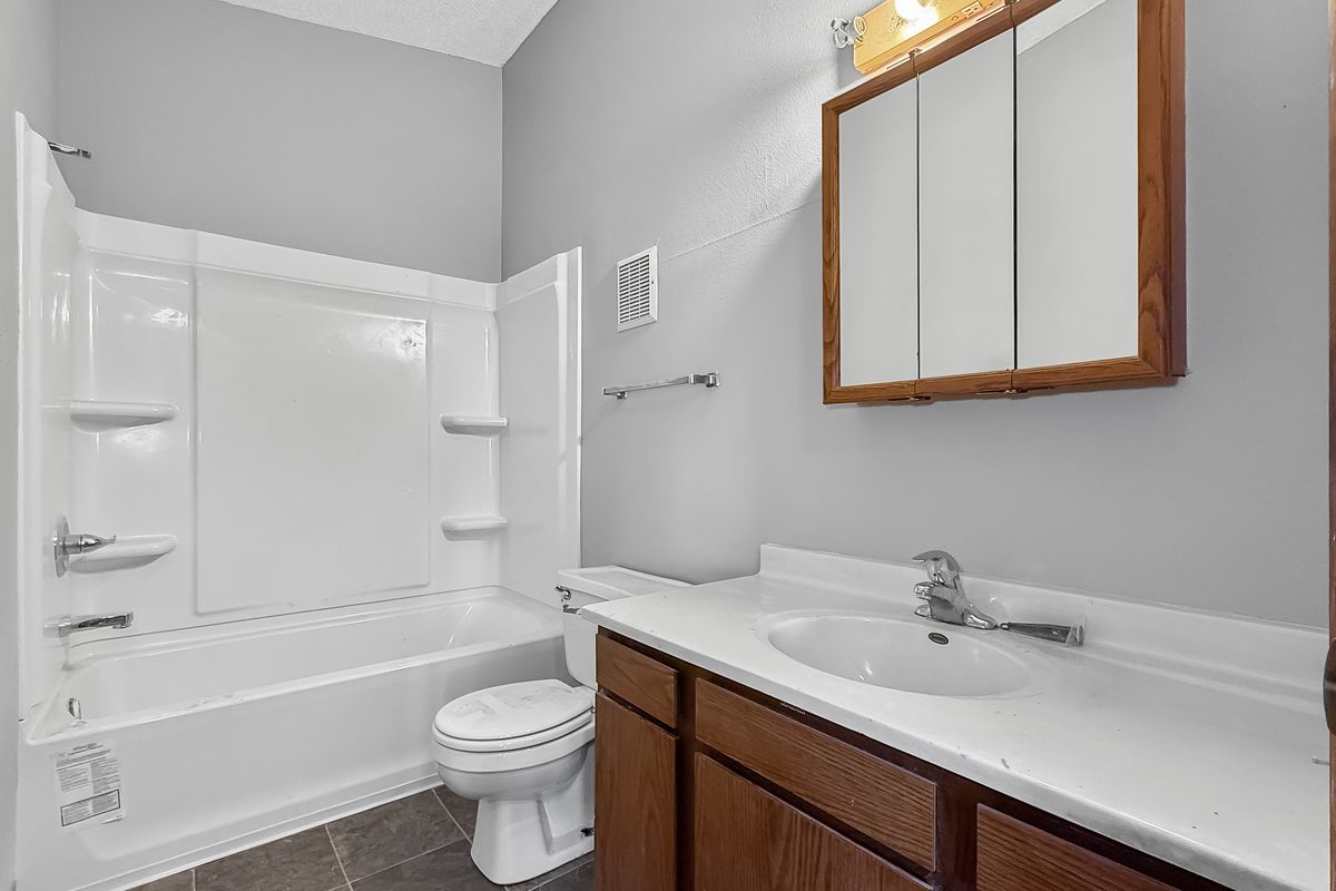 A bathroom with a tub and shower, a white toilet, an oak vanity with a white top and a mirrored medicine cabinet.