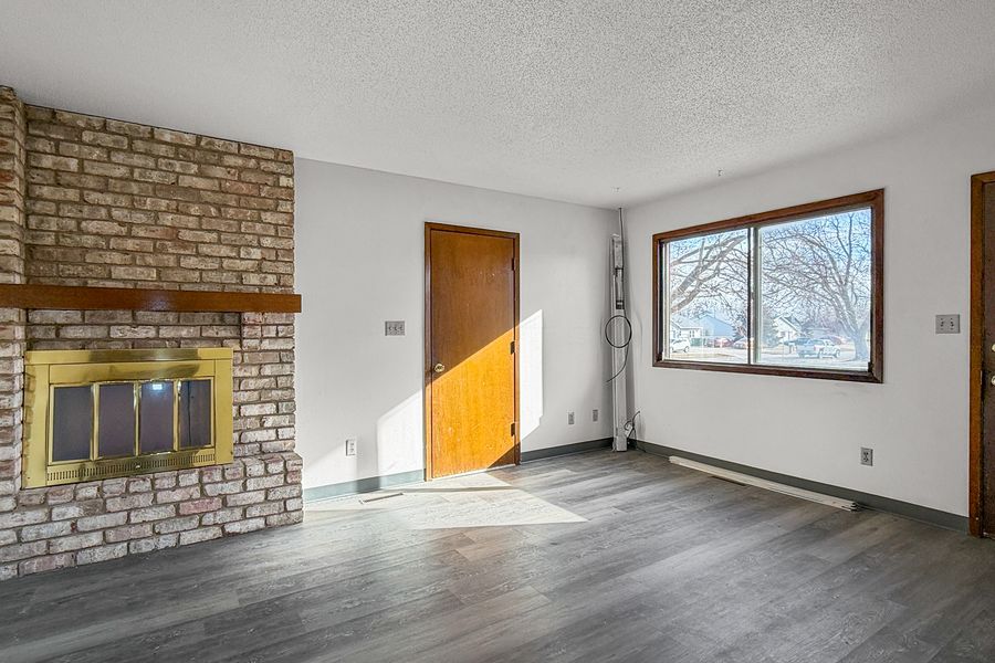 The living room of a townhome at East Park, with a brick fireplace, wood-look plank floor and a window to the lawn.